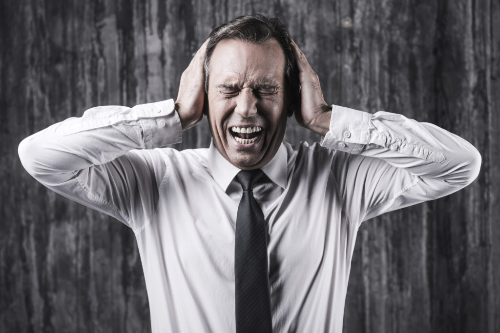 Emotional stress. Stressed mature man in shirt and tie holding head in hands and shouting while standing in front of dirty wall