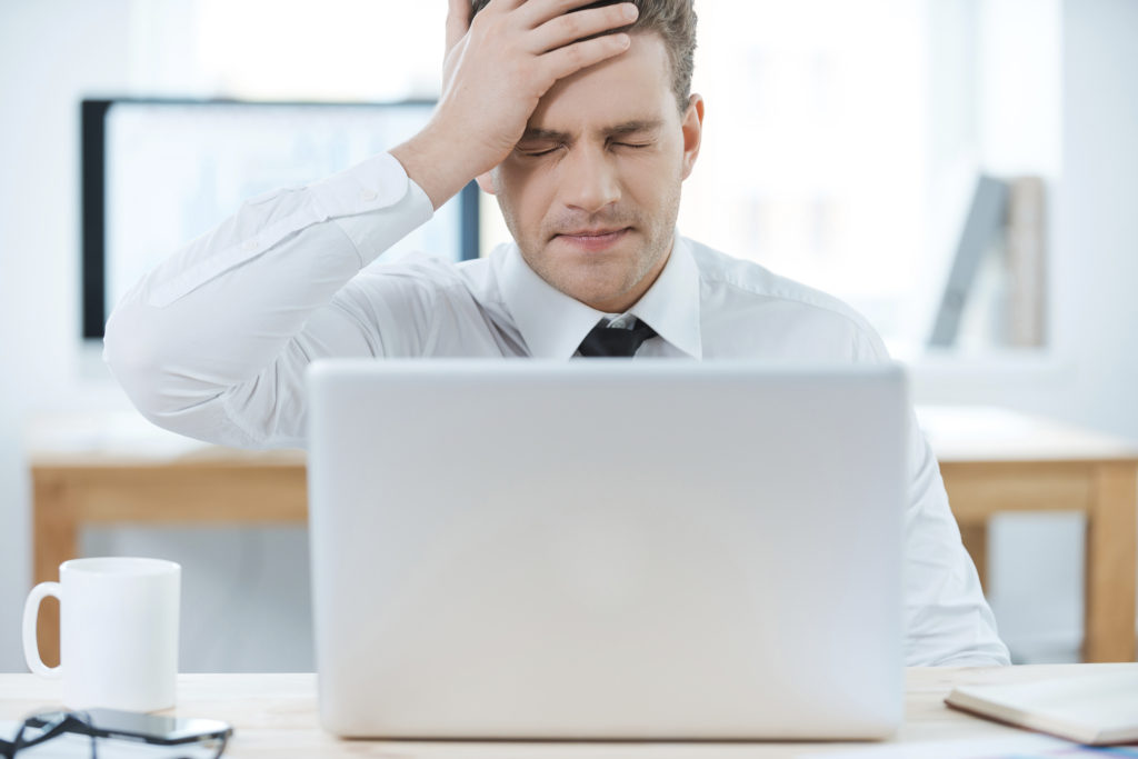 Oh no! Frustrated businessman working on laptop and touching his head while sitting at his working place